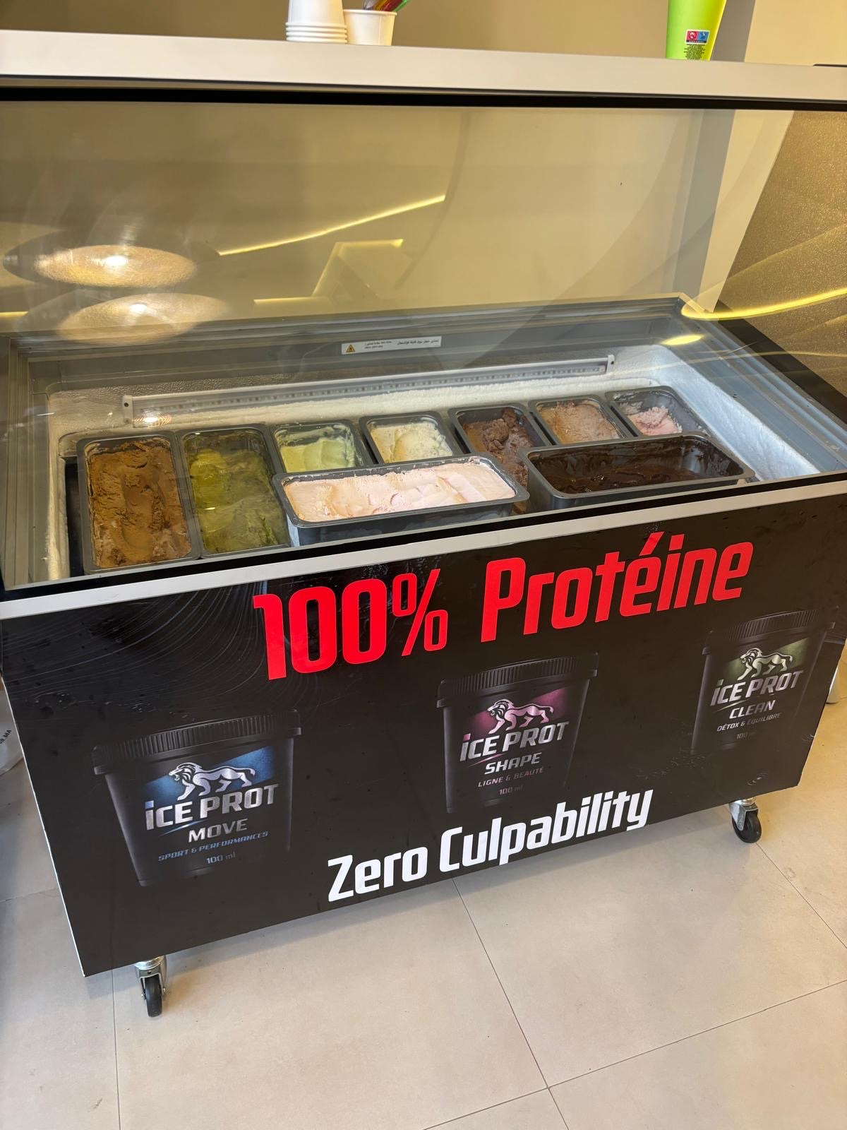 Vitrine glaces protéinées ICE PROT chez Chocolathé Marrakech — bacs de glaces aux parfums chocolat, matcha, pistache, vanille, fruits rouges, banderole 100% Protéine Zero Culpability
